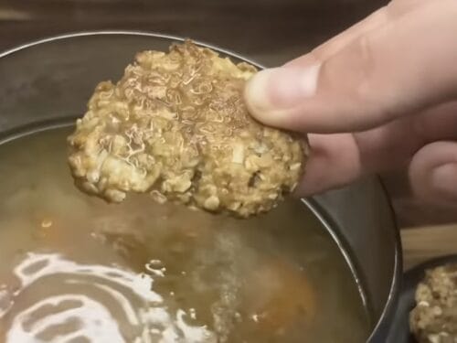 Hand holding a round oat biscuit above a pot of broth